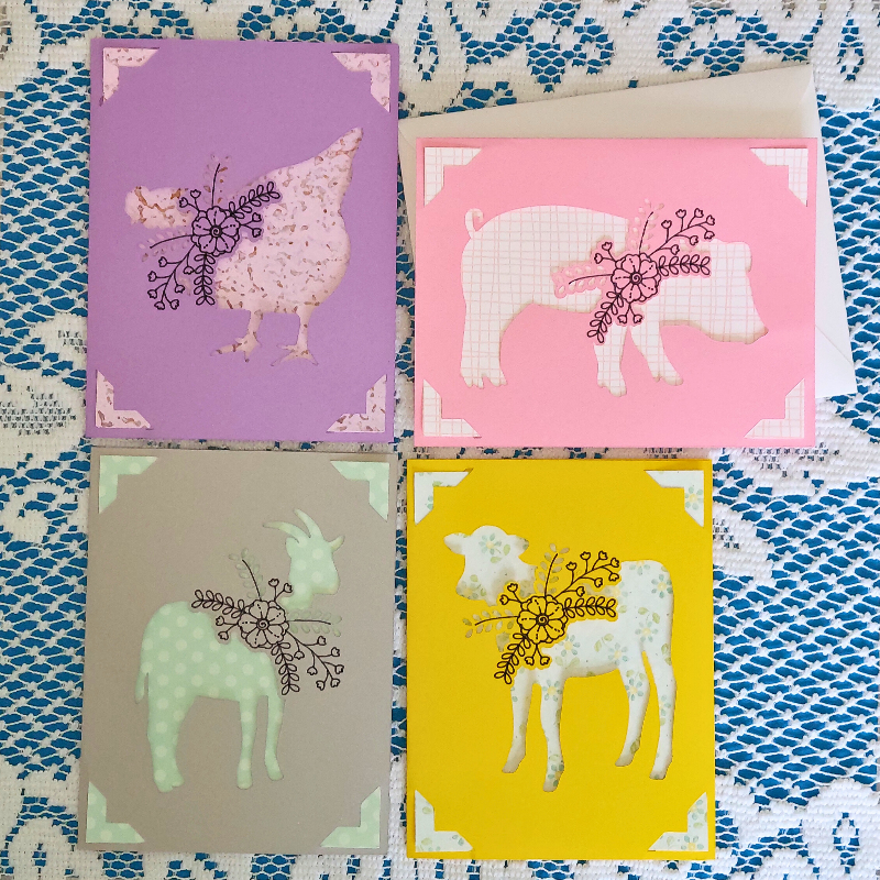Four greeting cards with animal illustrations on a patterned fabric background