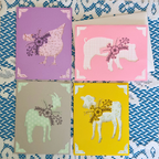 Four greeting cards with animal illustrations on a patterned fabric background
