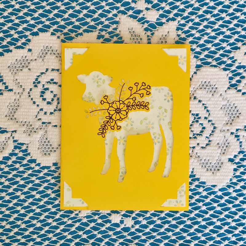 Yellow card with a white cow design on a textured blue and white surface