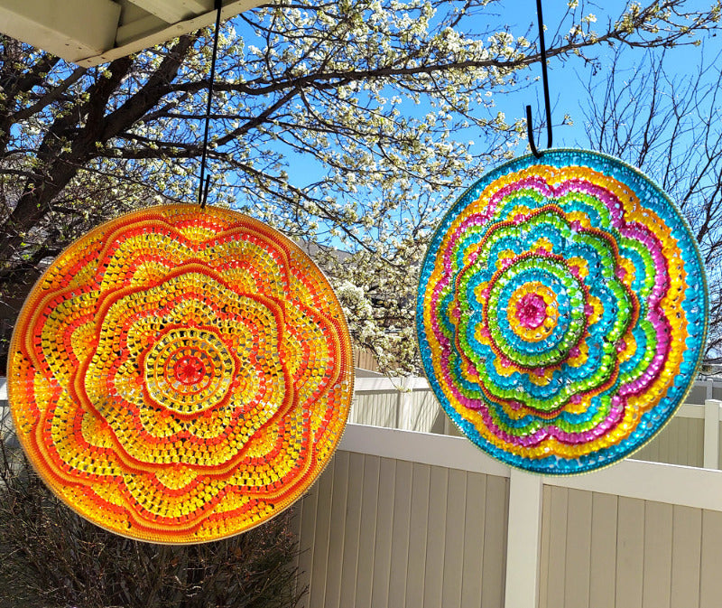 Two colorful circular mandalas hanging outdoors with trees and blue sky in the background.