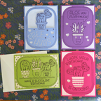 Four colorful greeting cards with succulent illustrations on a floral background