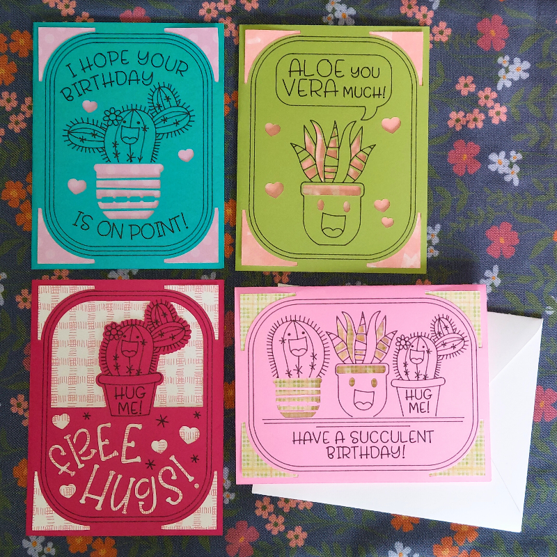 Four colorful greeting cards with succulent designs on a floral fabric background.