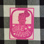 Pink card with a cactus illustration and 'Hug Me! Free Hugs!' text on a checkered fabric background.