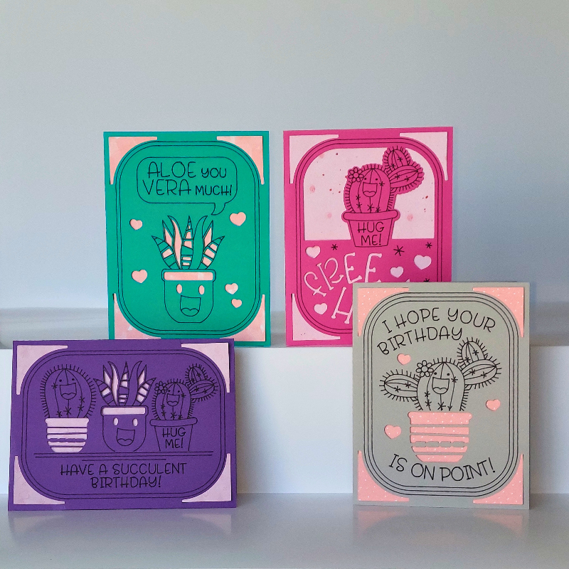Four colorful greeting cards with cactus illustrations and humorous text on a white surface.